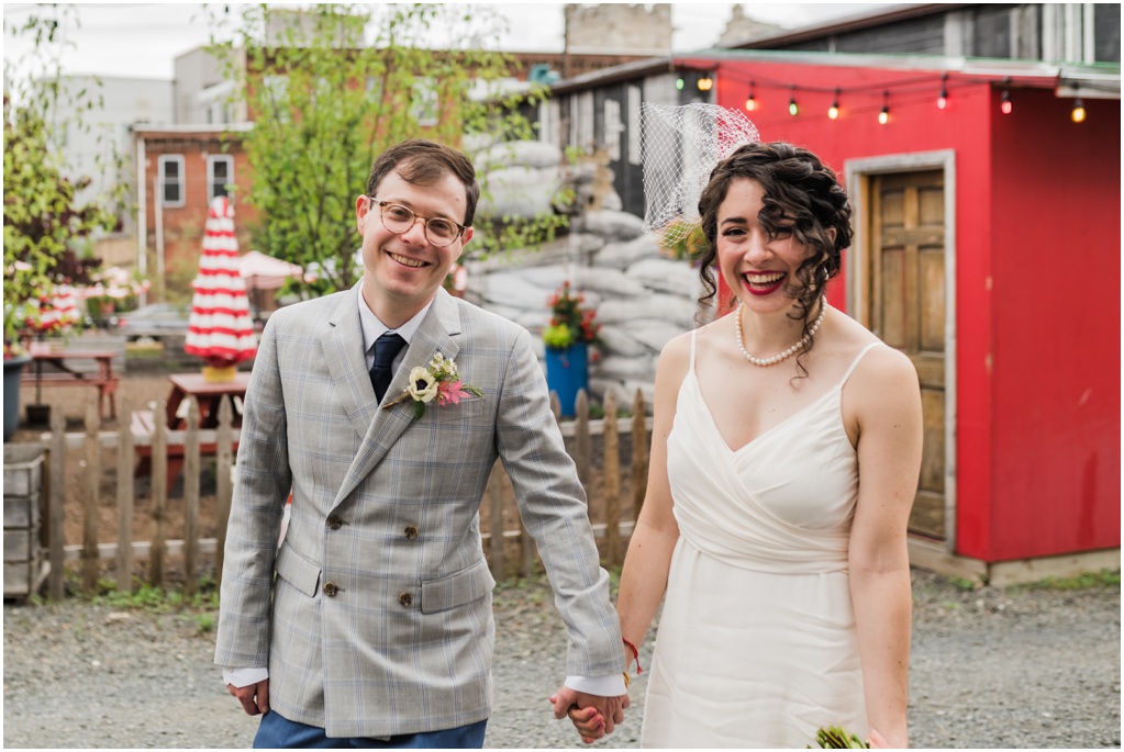 The couple smiles at the camera with a colorful courtyard behind them