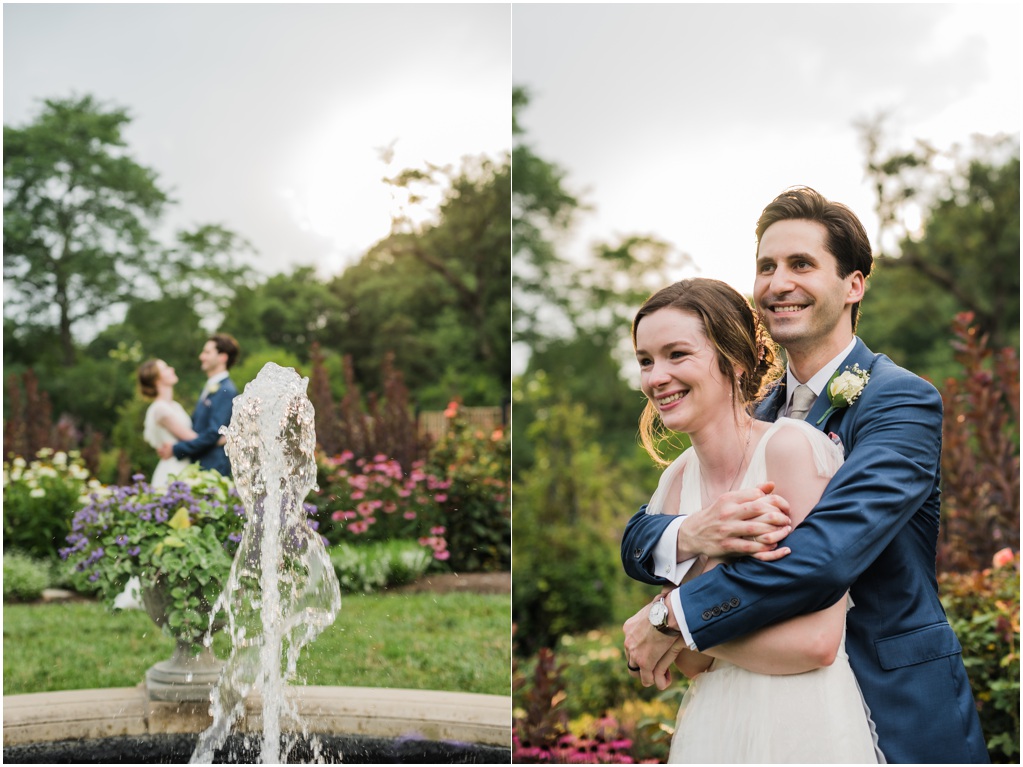 In the distance past a fountain, the couple embraces in the garden.