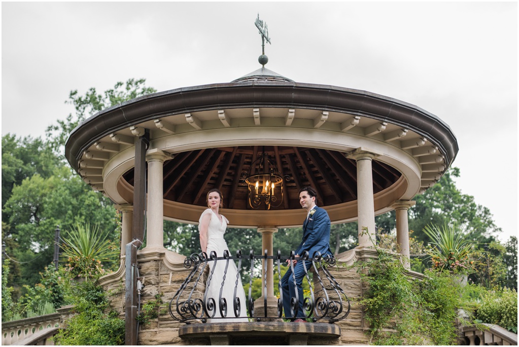 The couple stands under a gazebo and looks over the garden