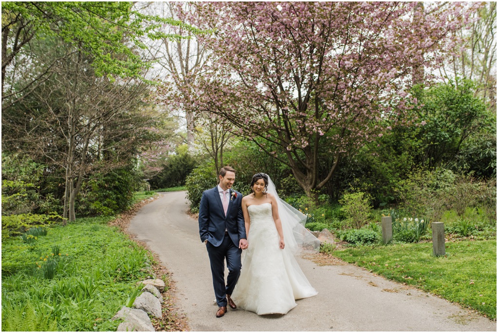 A bride and groom walk down a path near a blossoming cherry tree