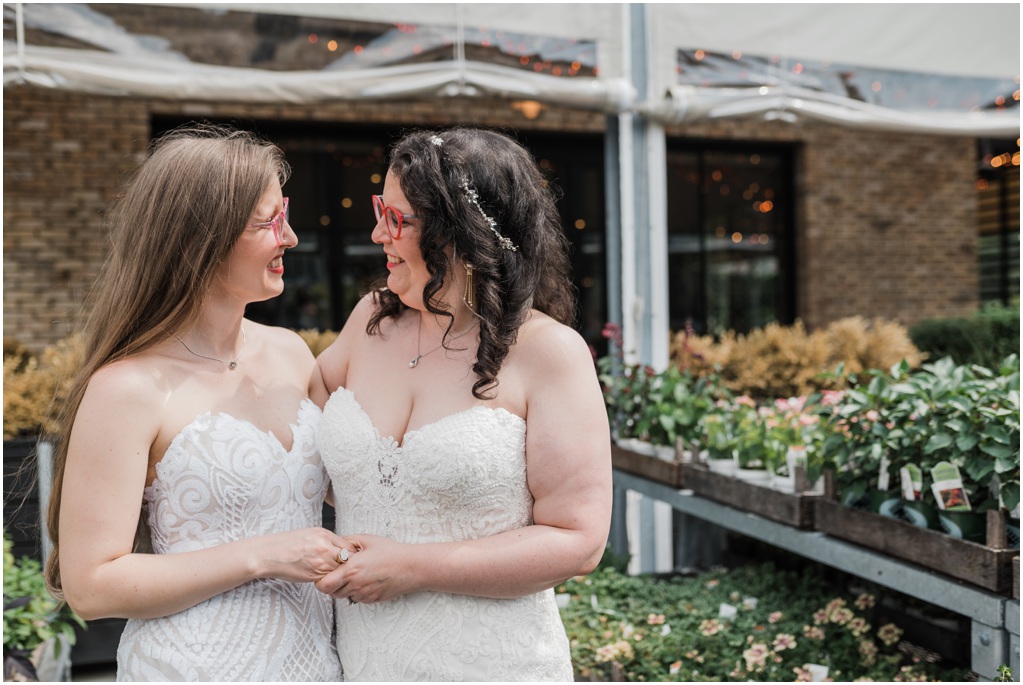 The brides hold hands near some flats of succulents