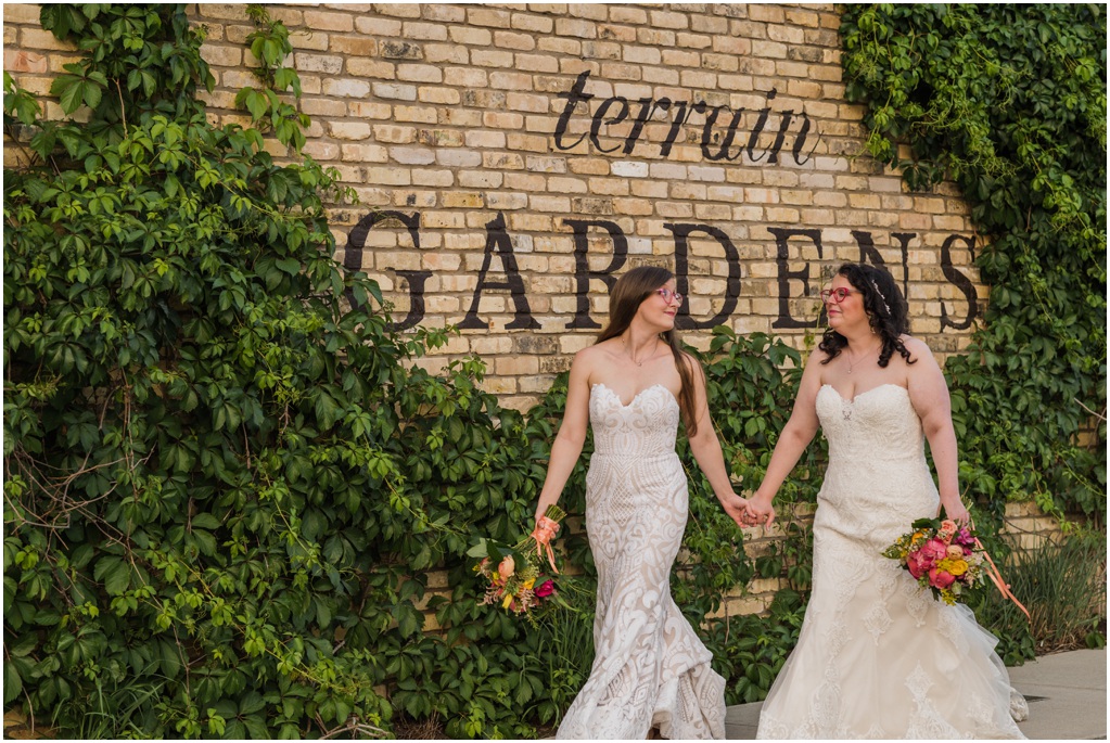 Two brides walk in front of the Terrain Gardens sign