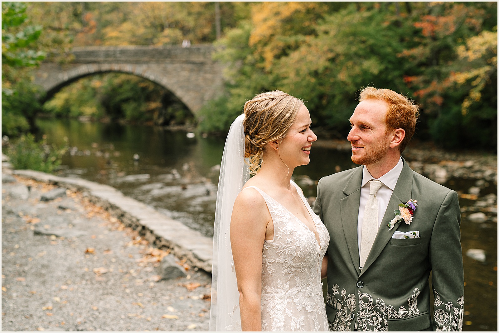 A bride and groom pose beside the Wissahickon Creek outside the Valley Green Inn.