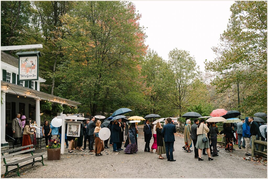 Wedding guests walk towards a ceremony carrying umbrellas.