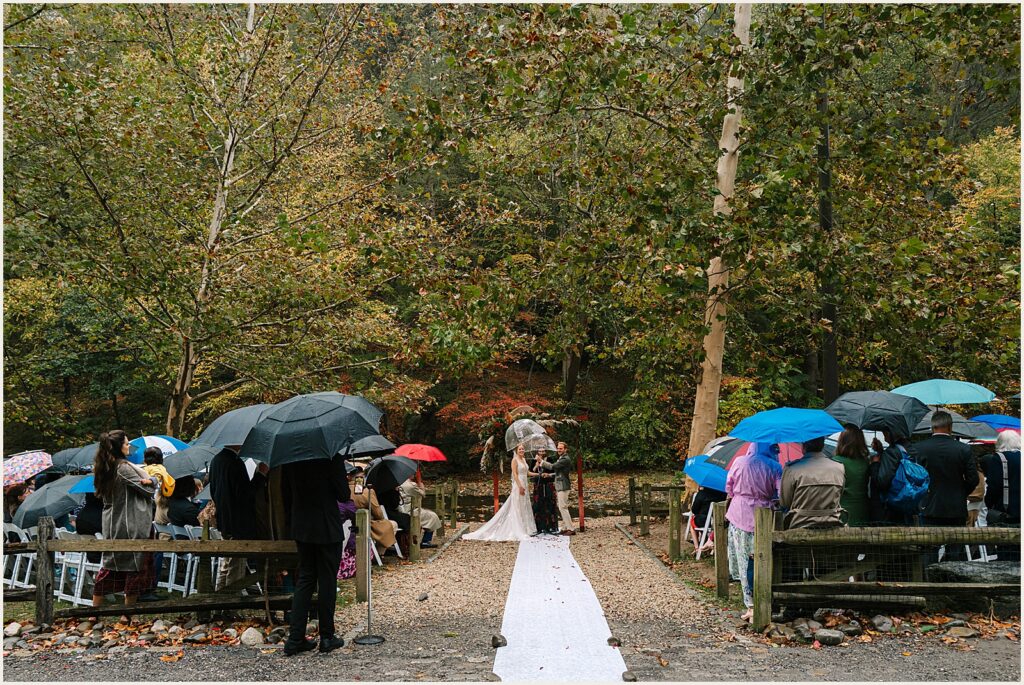 Wedding guests hold umbrellas during a rainy day wedding ceremony.