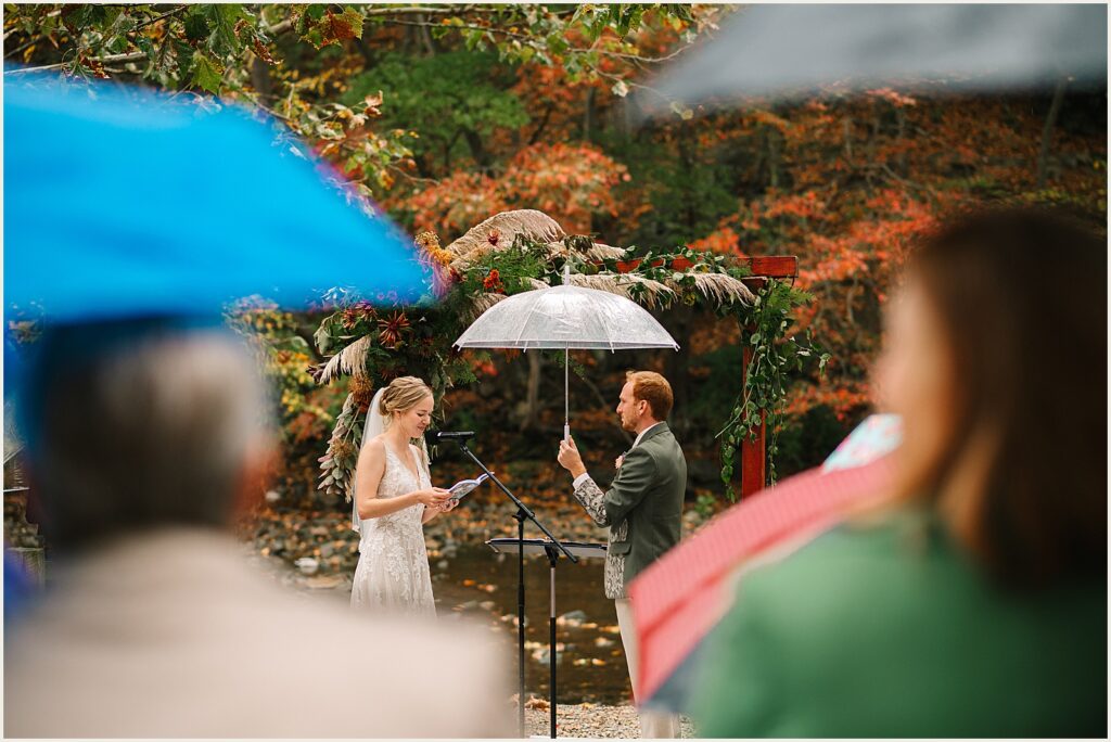 A groom holds an umbrella over a bride during a wedding ceremony.