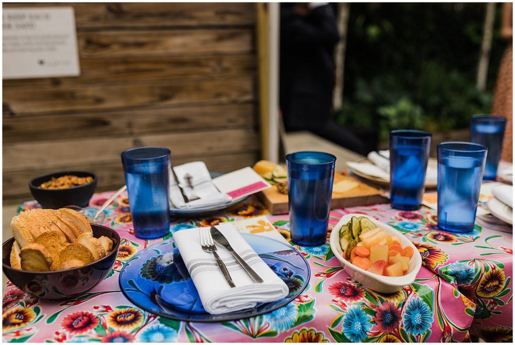 Blue plates and glasses sit on a colorful wedding table with appetizers.