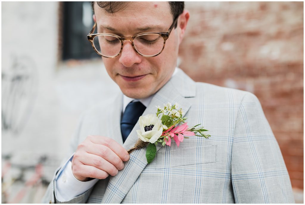 A groom looks at his pink, white, and green boutonnière. 