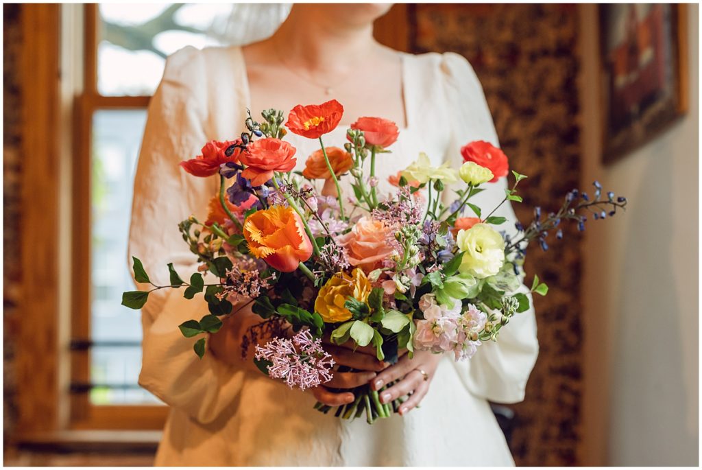 A bride holds a bouquet with orange, pink, and yellow flowers.