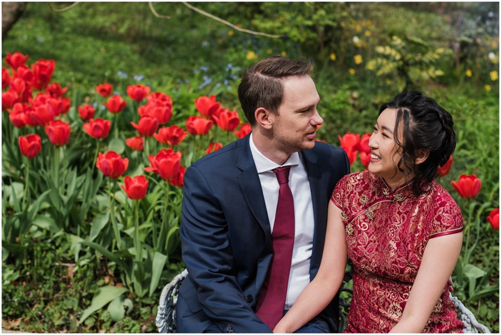 A couple sits in front of a garden of red tulips.