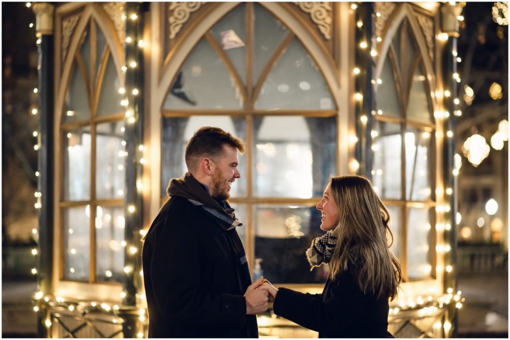 A woman smiles after her Rittenhouse Square proposal surrounded by holiday lights.