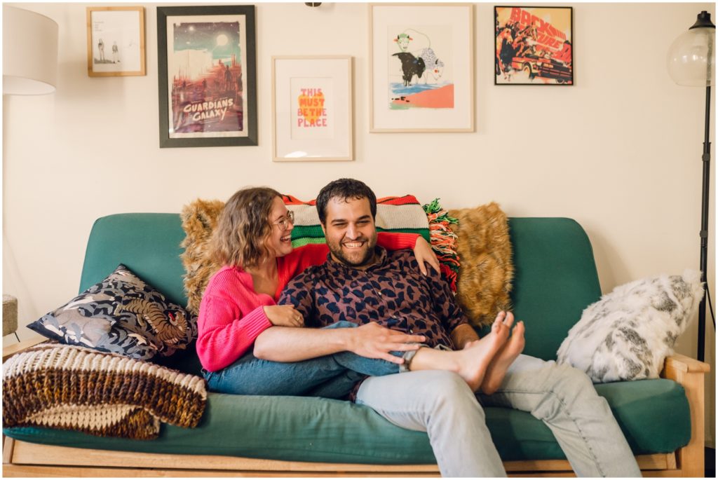 A man and woman sit on a couch during at home engagement photos in Philadelphia.