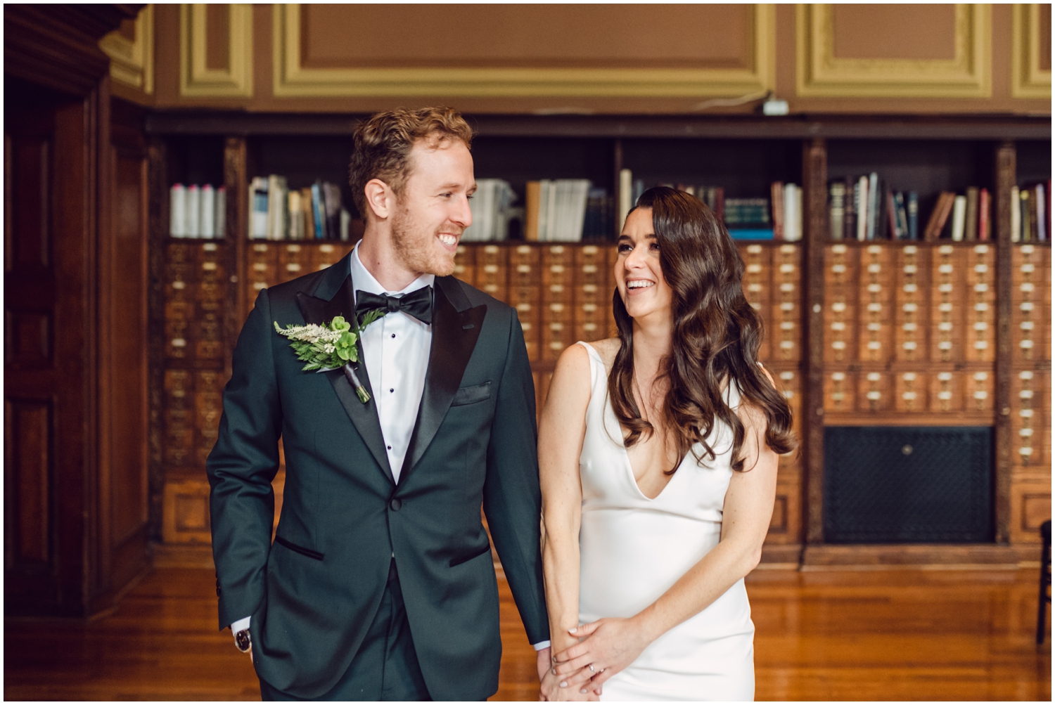 A bride and groom hold hands in front of a row of card catalogs at a Mutter Museum wedding.
