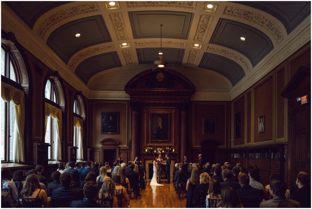 A Mutter Museum wedding ceremony takes place in a high-ceilinged room with blue and white paint and dark wood walls.