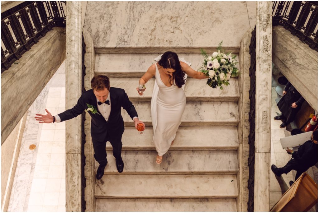 Kristen and Jack walk down the wide white marble staircase to the cocktail hour.