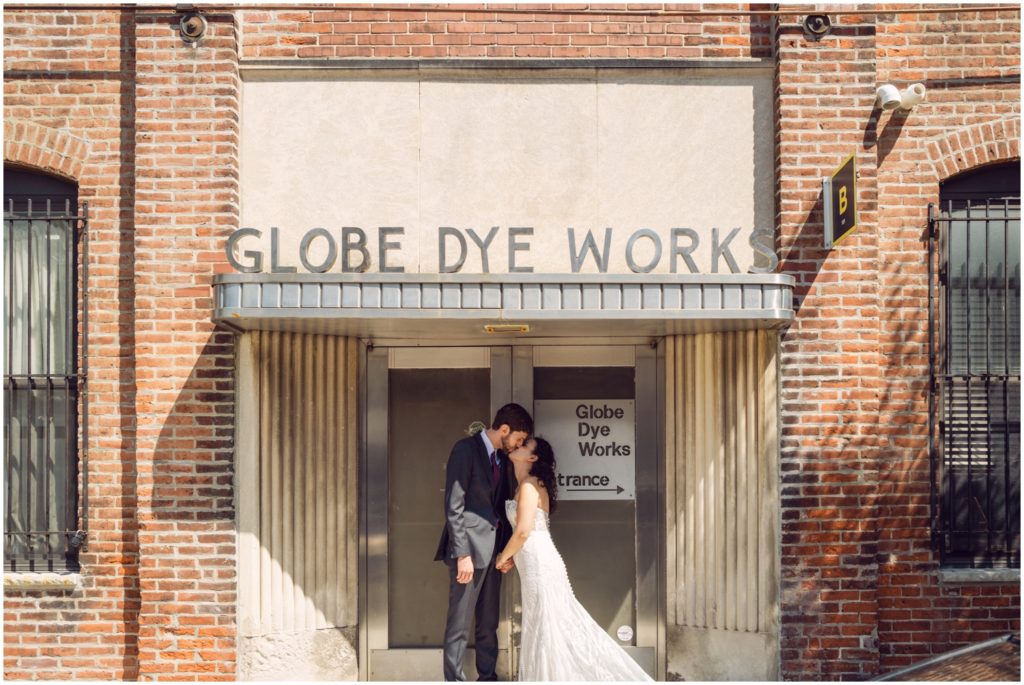 A bride and groom kiss in front of the Globe Dye Works building.