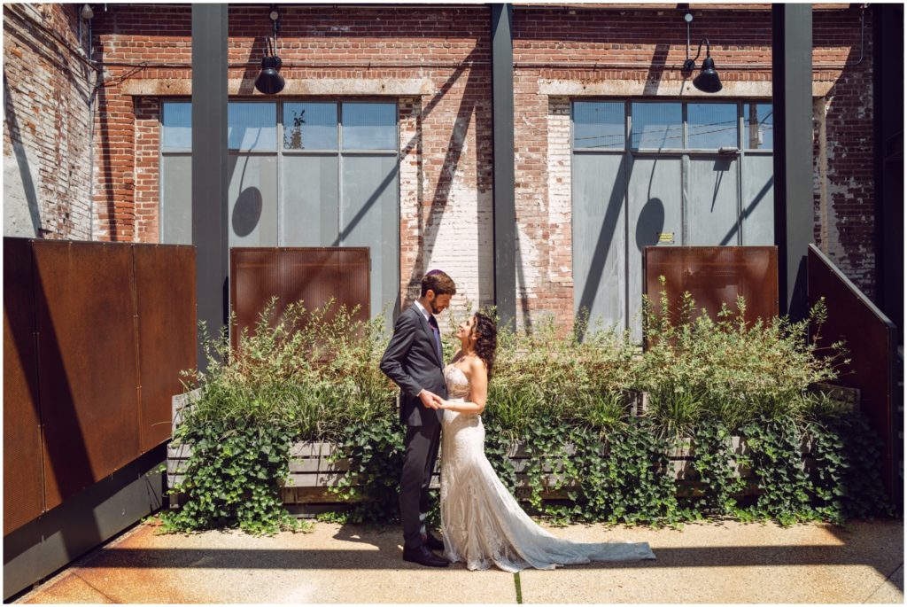 The bride and groom pose in the Globe Dye Works courtyard in front of full planters.