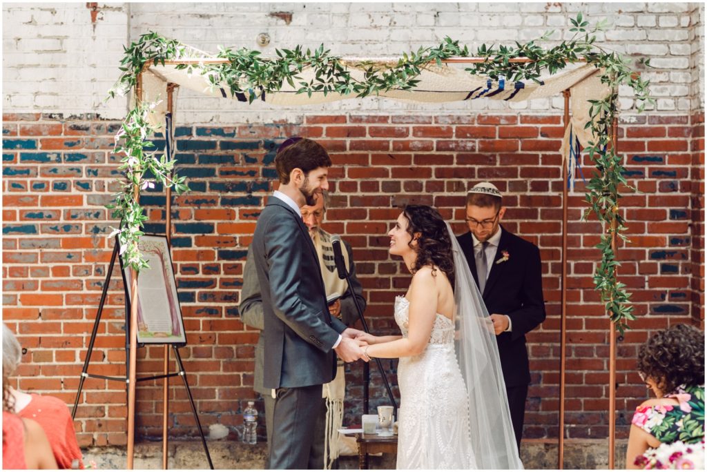 Eliana and Marcus hold hands under a floral chuppah.