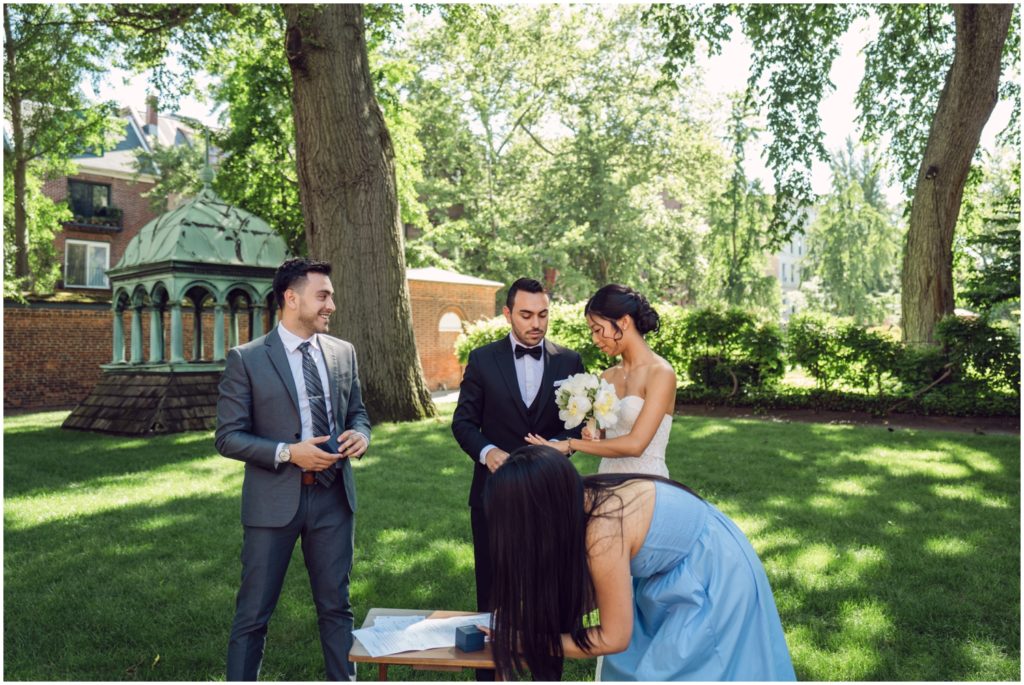 A bridesmaid signs a marriage license beside a bride and groom as an alternative to a wedding.
