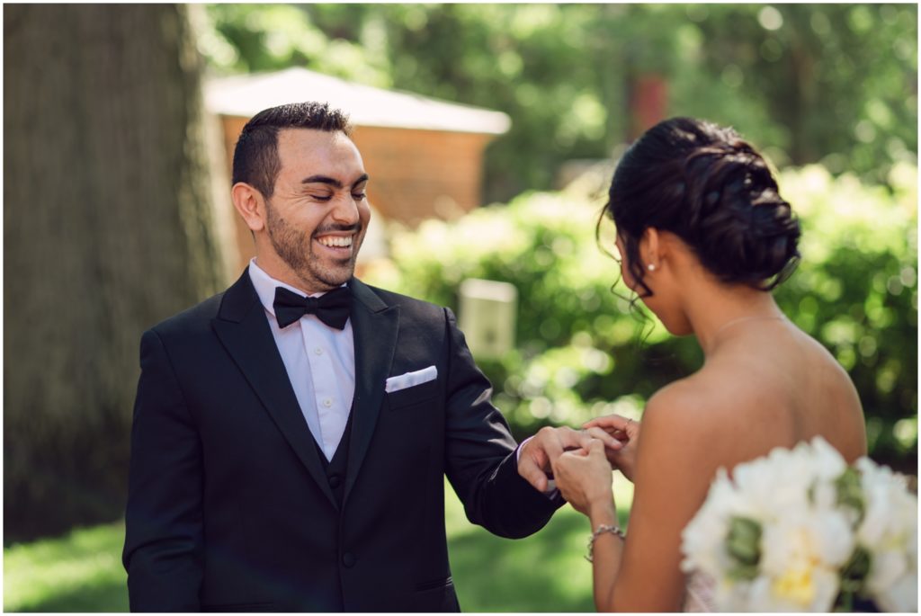 A groom laughs as a bride puts a rink on his finger.