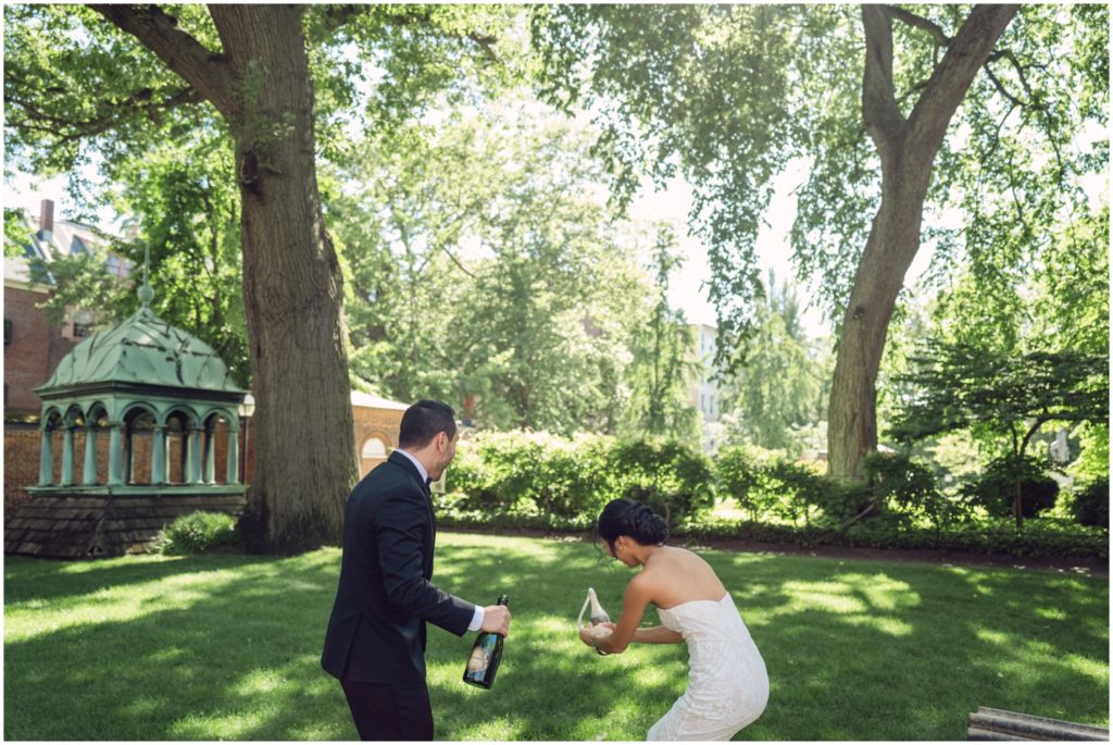 A bride and groom open champagne bottles in Penn's Hospital Gardens.
