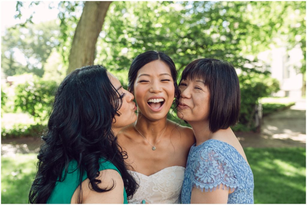 Family members stand on either side of a bride and kiss her cheeks.