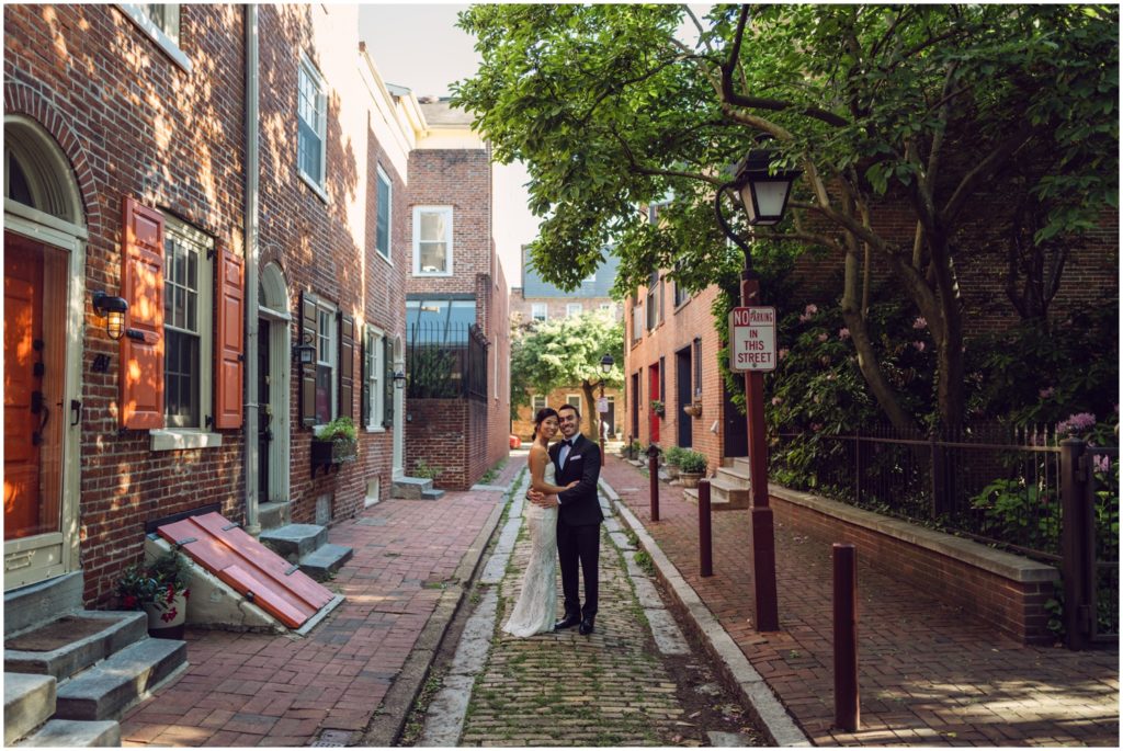 A bride and groom stand in the middle of a narrow cobblestone street.