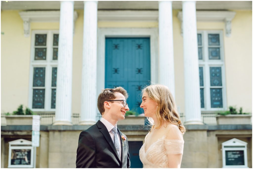 A bride and groom stand in front of a Philadelphia building with white pillars and a blue door.
