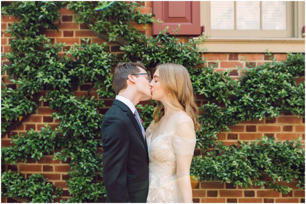A couple kisses in front of an ivy covered brick wall before their Hill Physick House wedding.