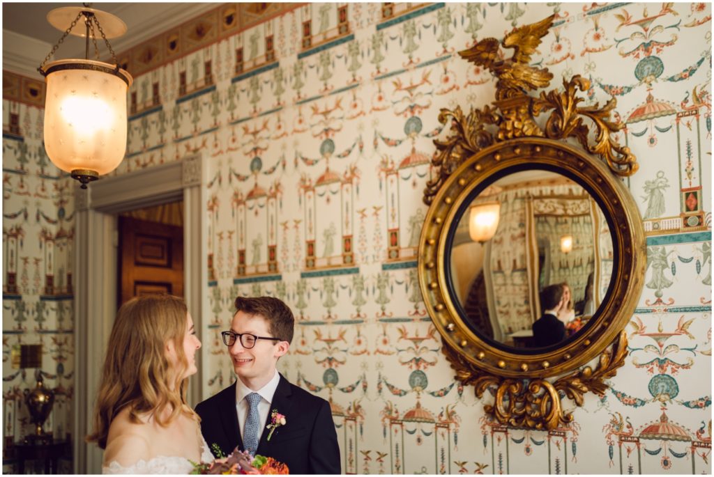 An antique mirror in the Hill Phsyick House reflects a bride and groom in the entrance hall.