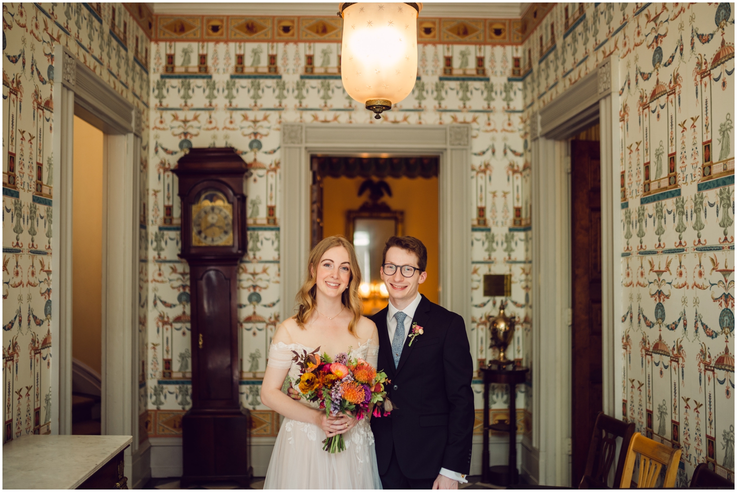 A bride and groom pose in the entrance hall at their Hill Physic House wedding.