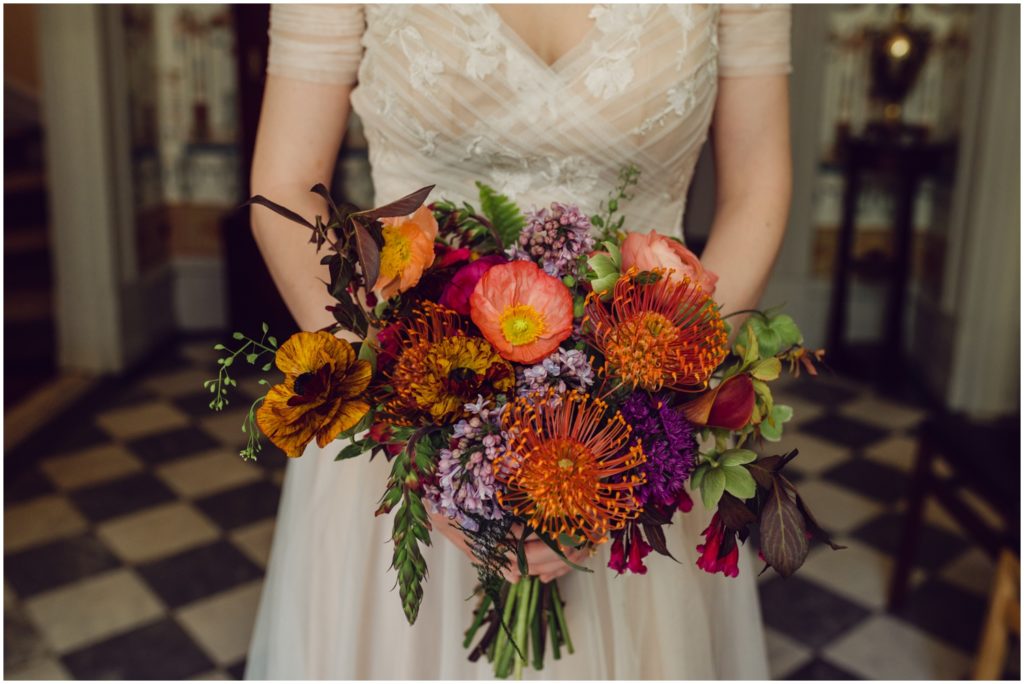 A bride holds a bouquet with pink, orange, and purple flowers.