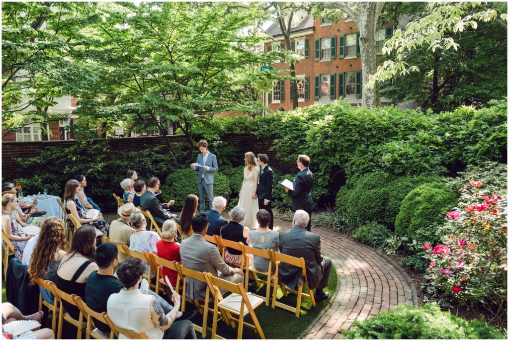 Wedding guests sit in the garden on wooden chairs for the Hill Physick House wedding ceremony.