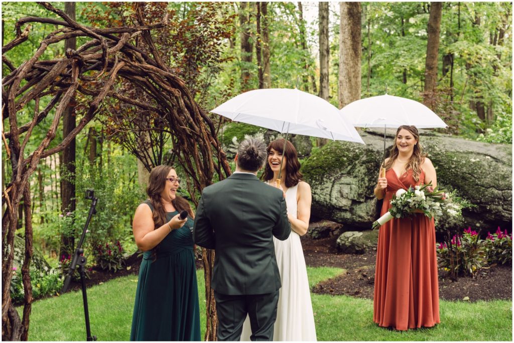A couple and their wedding party hold matching umbrellas for a rainy day wedding ceremony.