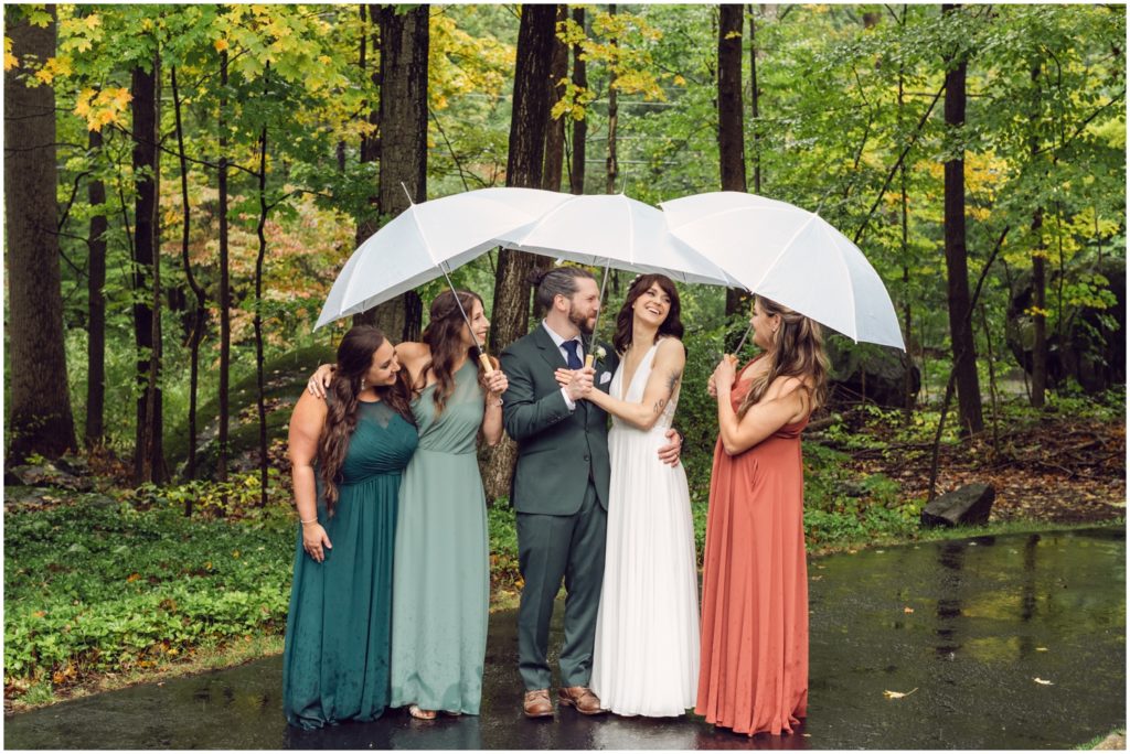 A bride and groom pose with friends under white umbrellas.