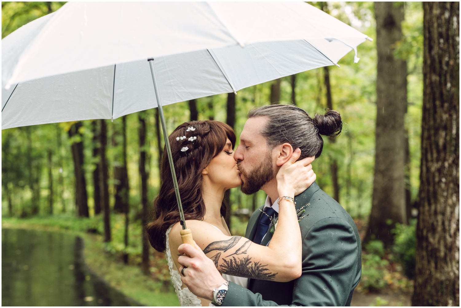 A bride and groom kiss under an umbrella at a rainy day wedding.