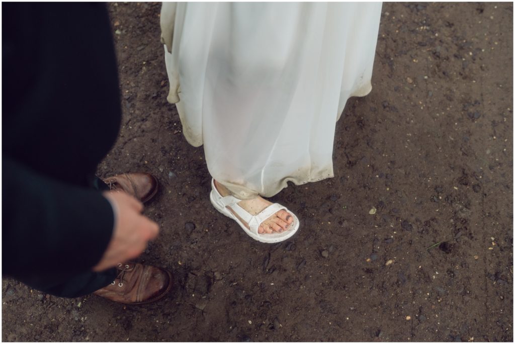 A bride lifts the muddy hem of her skirts to show her white Tevas sandals.