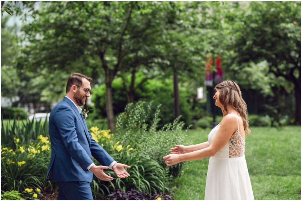 A bride and groom have a first look on the Ben Franklin Parkway beside a yellow flower garden.