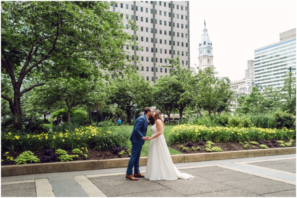 A bride and groom kiss with Philadelphia City Hall in the background.