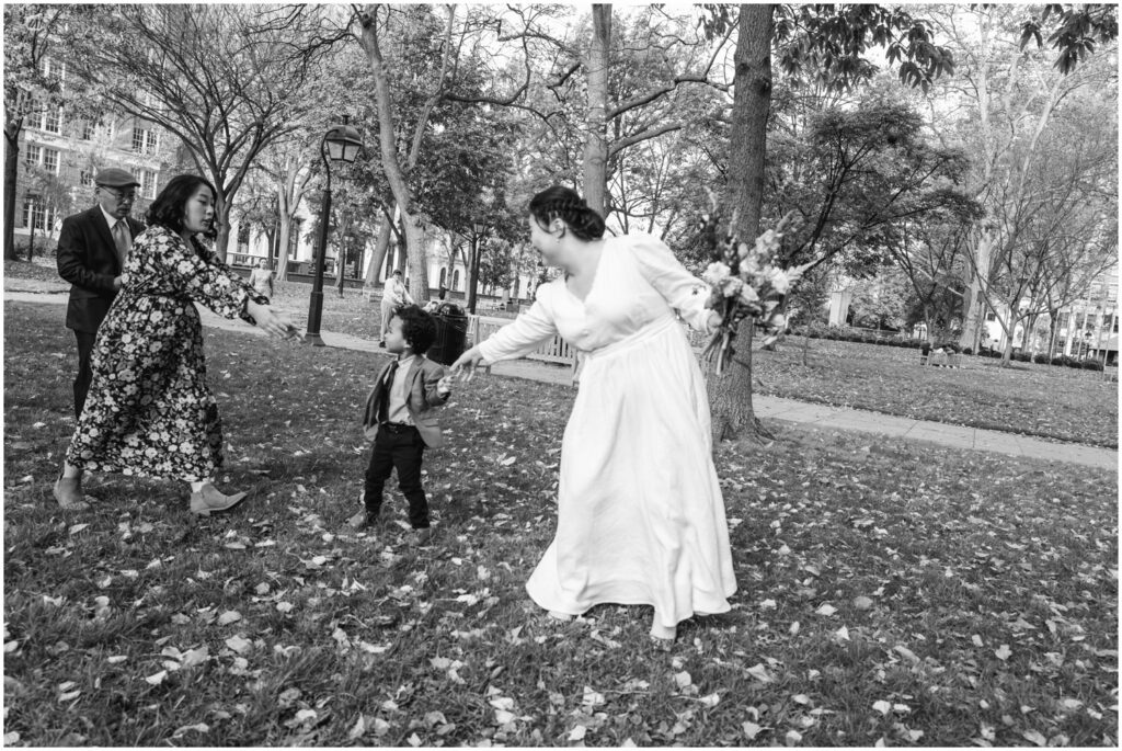 A bride reaches towards a child running through a park.