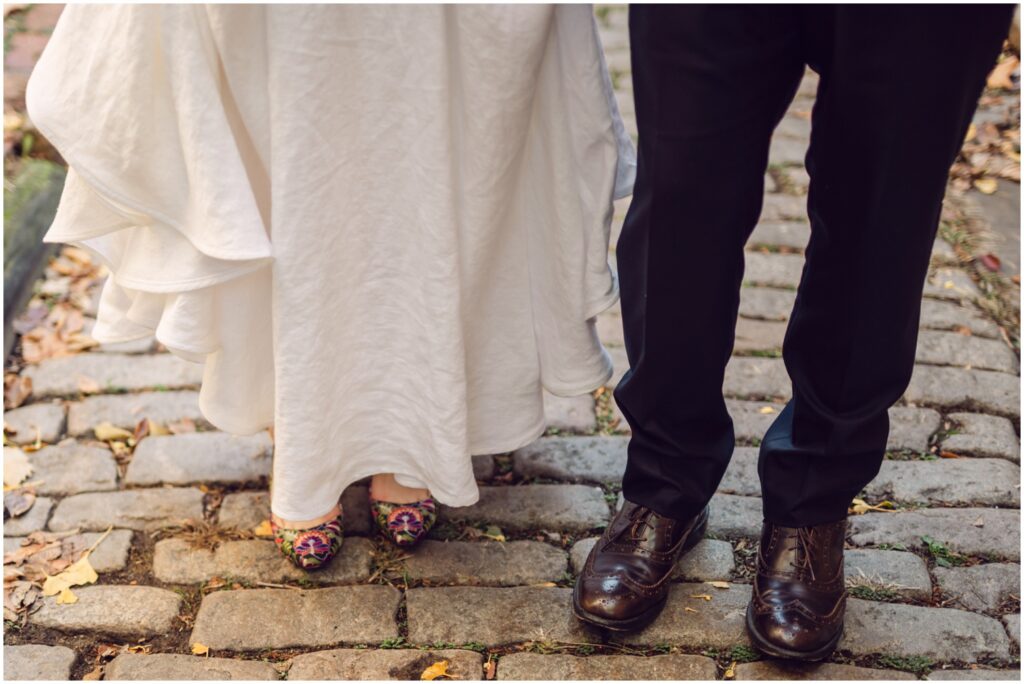 A bride and groom stand side by side showing their wedding shoes to a Philadelphia wedding photographer.
