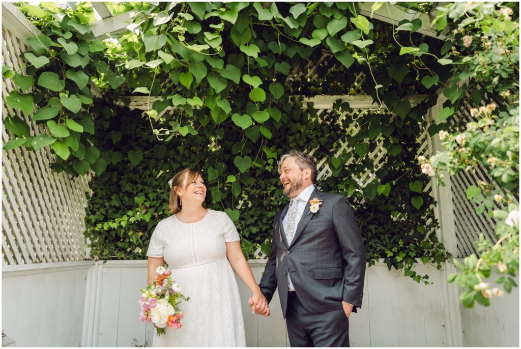 A bride leads a groom by the hand down a garden path.