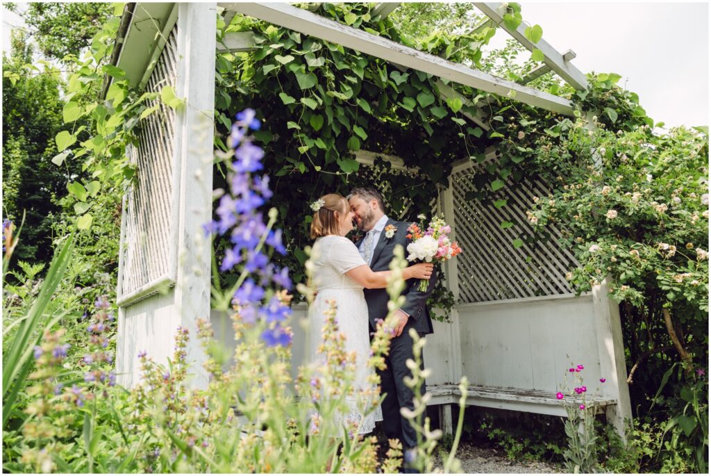 A bride and groom stand under a shelter in the garden at Wyck House.