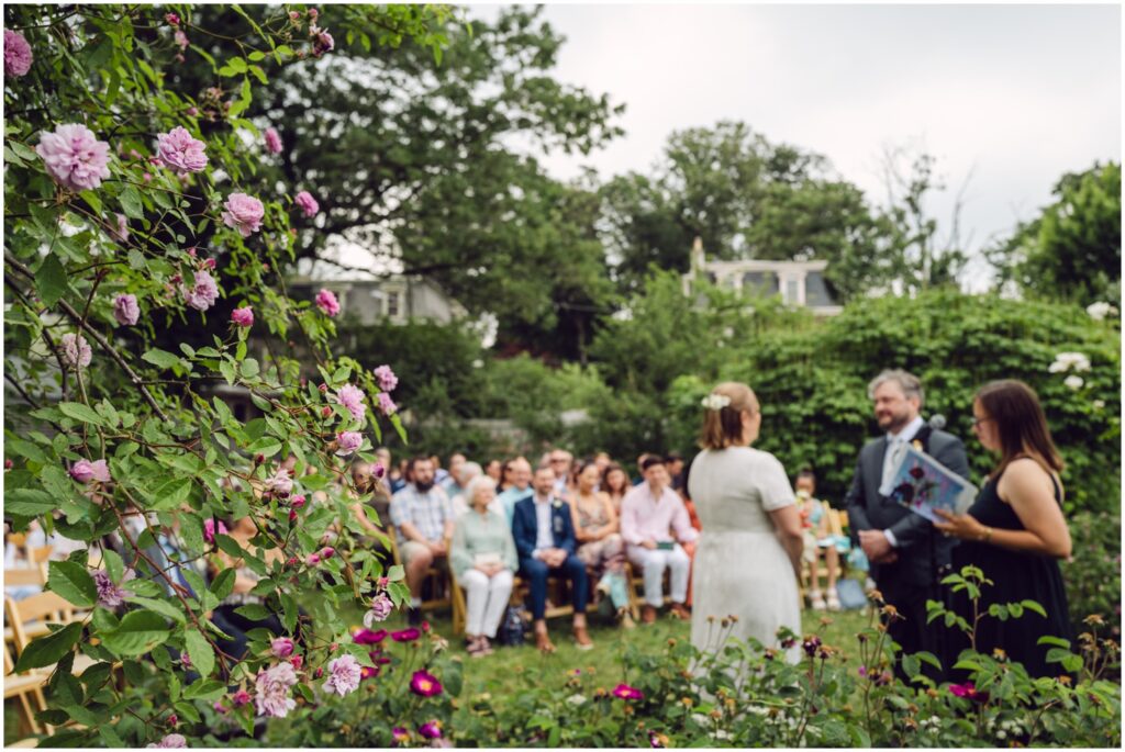 Wedding guests watch a bride and groom exchange vows in the Wyck House garden.