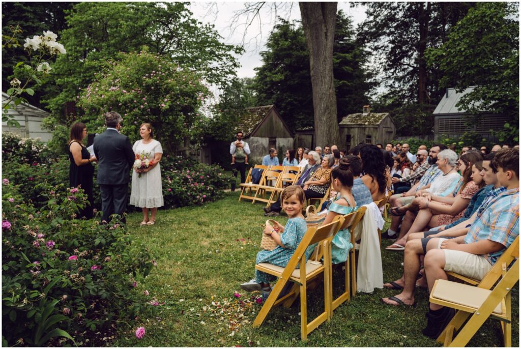 Guests sit in wood chairs to watch the Wyck House wedding.
