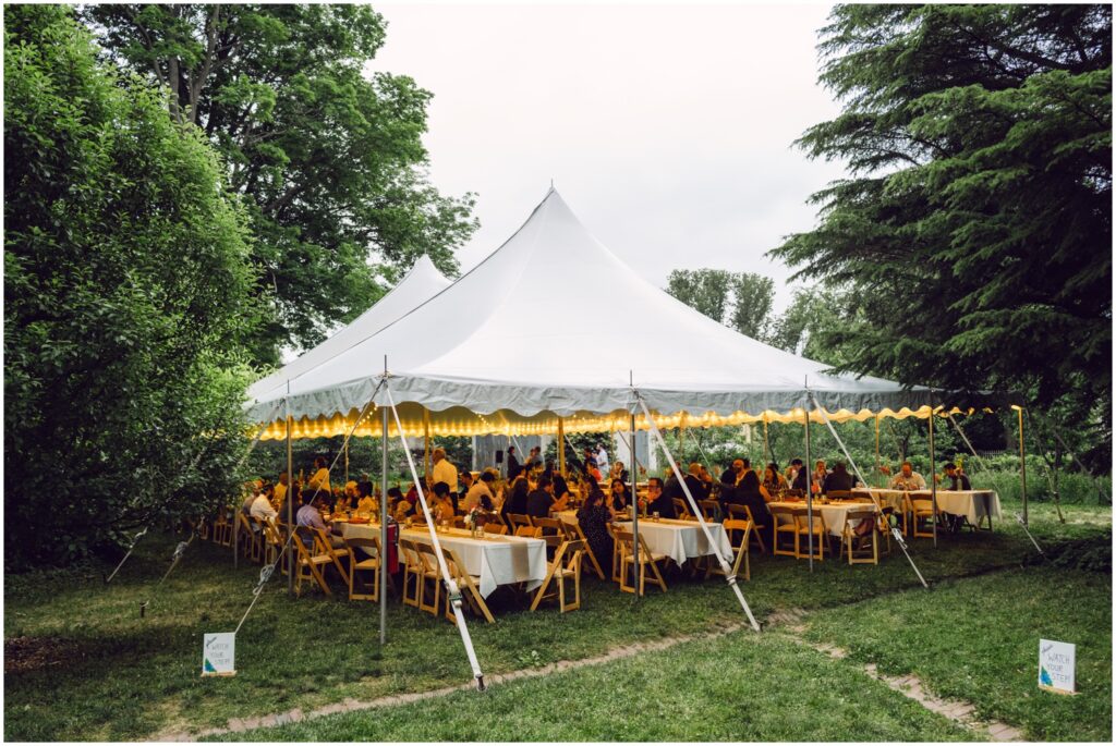 A wedding reception takes place under a white tent strung with lights.