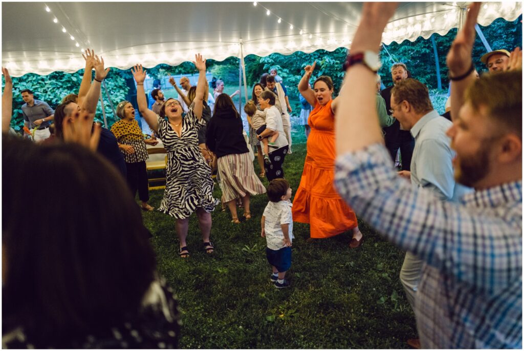 Wedding guests throw their hands up while they dance.