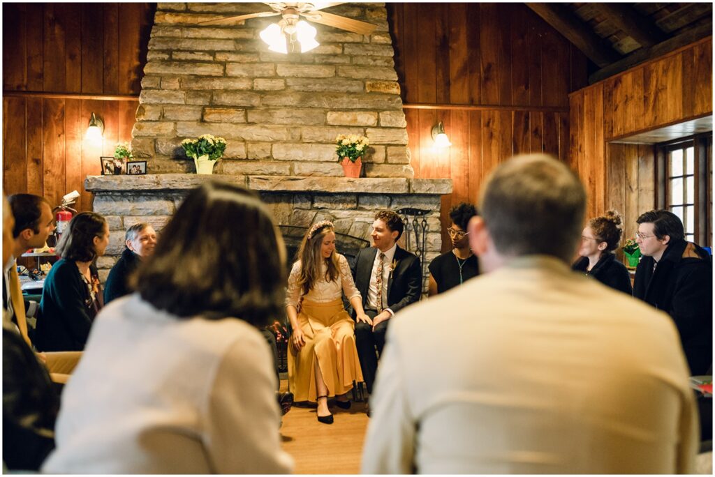 A bride and groom hold hands sitting beside each other during their Quaker wedding ceremony.