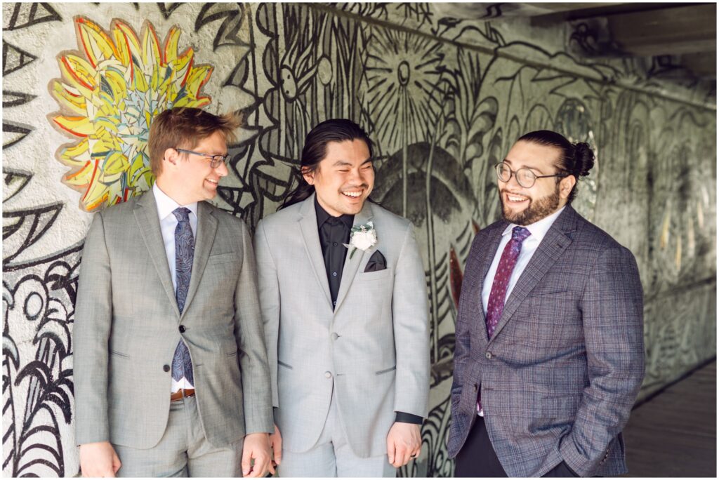 A groom poses beside a Philadelphia mural with two friends.