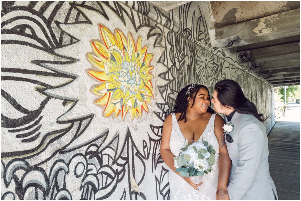 A groom kisses a bride's cheek beside a mural at their Philadelphia elopement.
